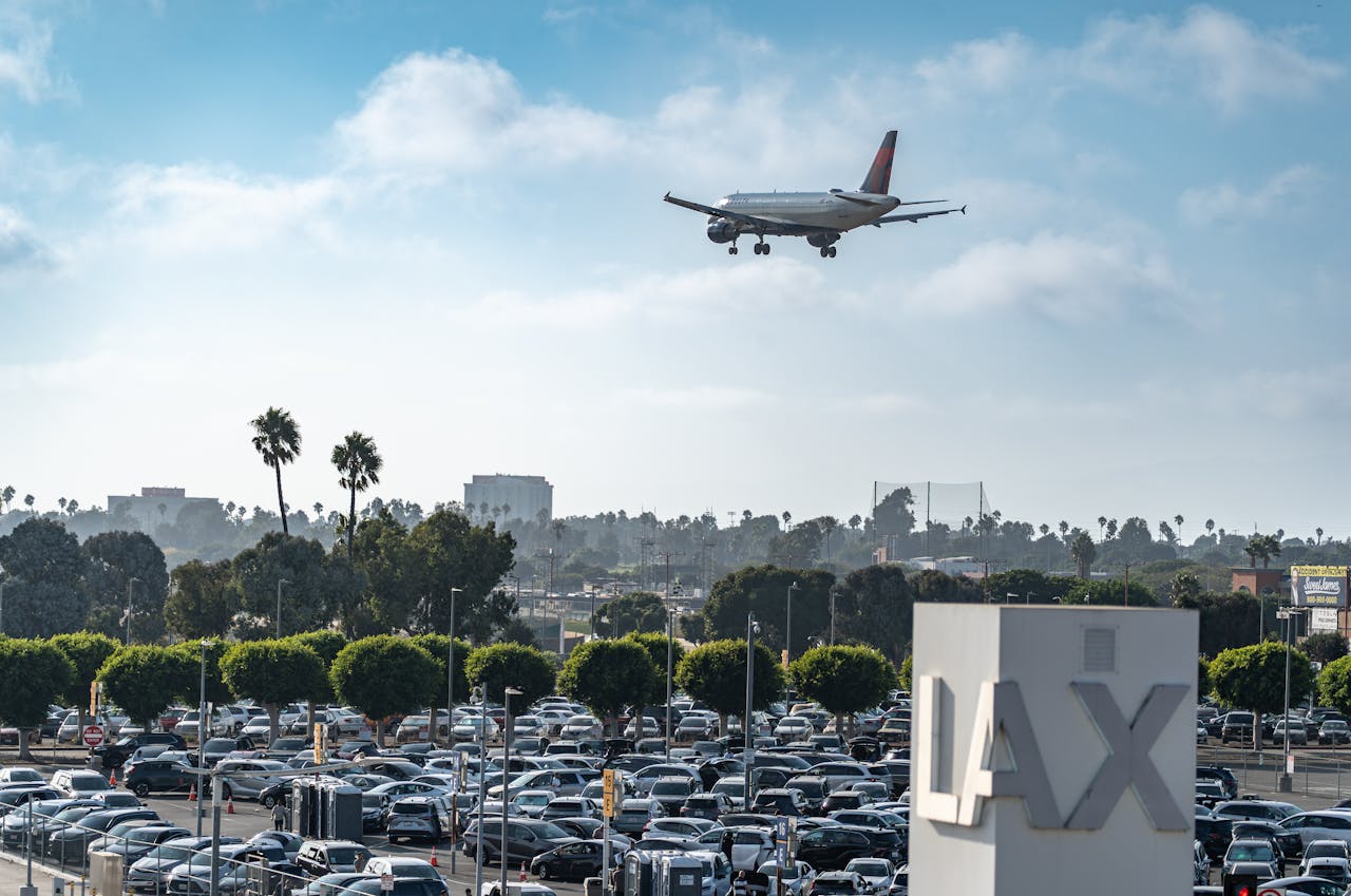 Airplane landing over LAX airport parking with cityscape and blue skies.